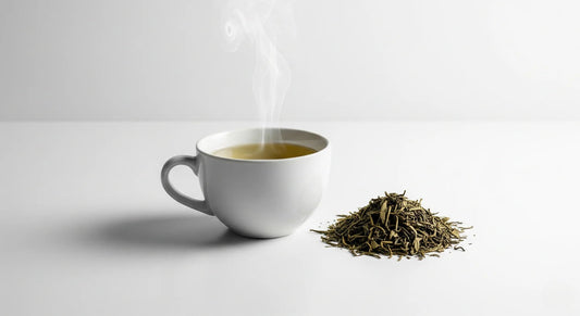 White mug with steaming tea and a pile of green tea leaves on a light gray background
