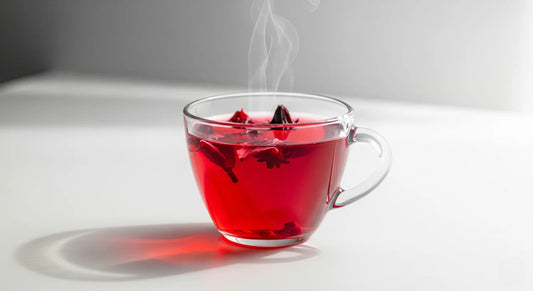 Clear glass mug with red liquid and steam on a white surface