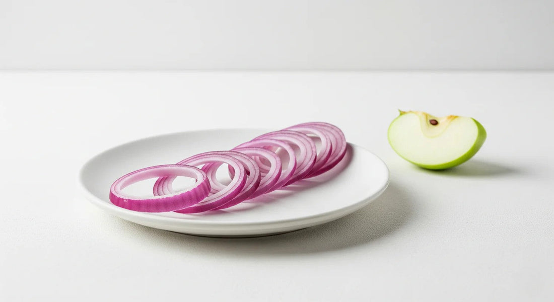 Sliced red onions on a white plate with a green apple half on a light gray background